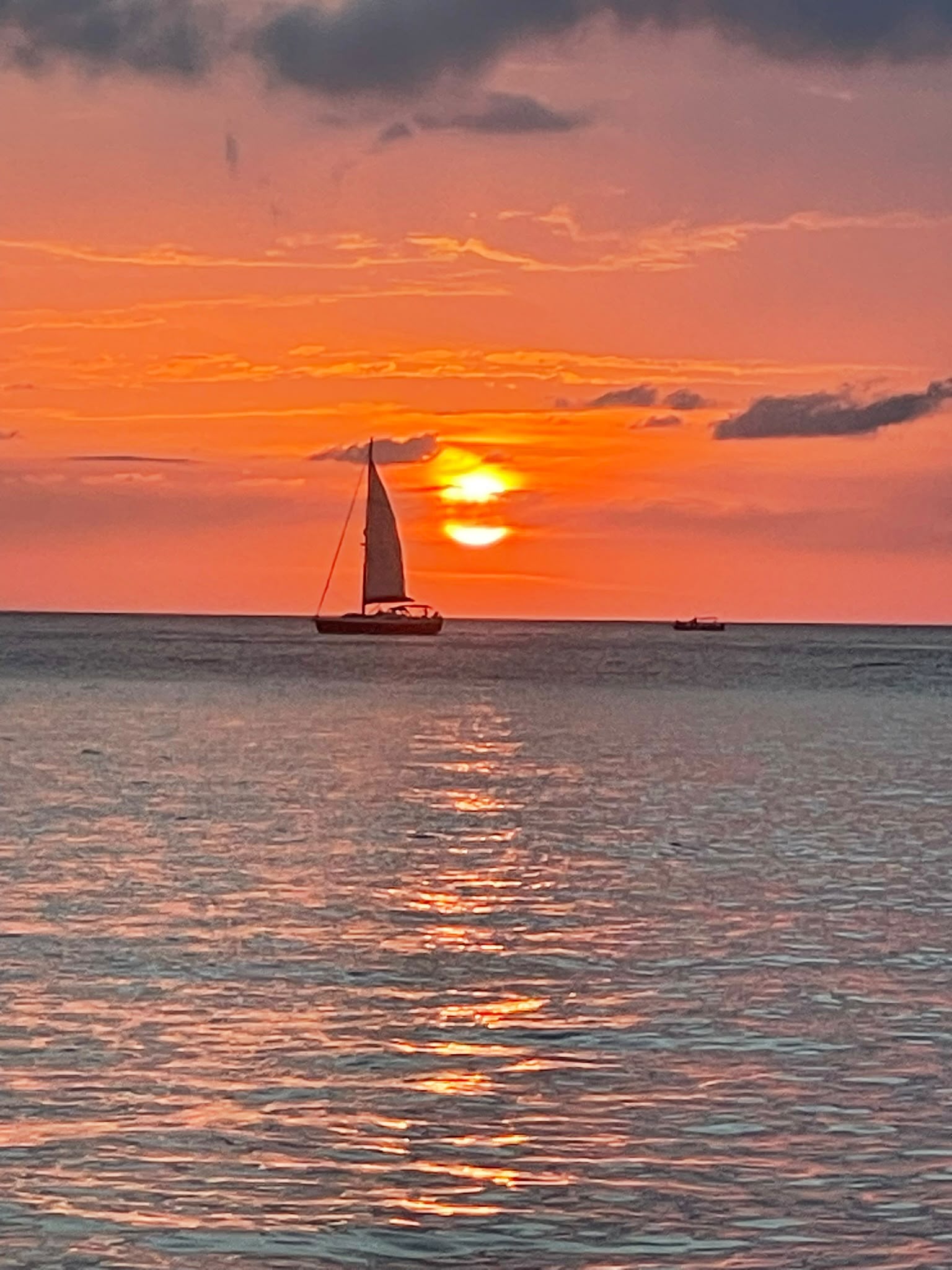 Velero cruzando frente a un sol anaranjado